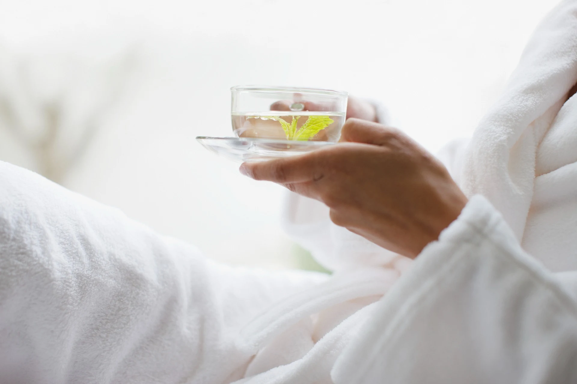 close up of woman in bathrobe holding cup of detox tea